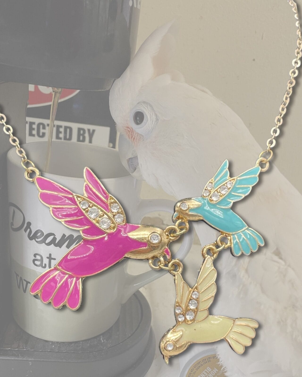 An Enchanting Enamel Trio of Hummingbirds Necklace with two parrots and a cup of coffee.